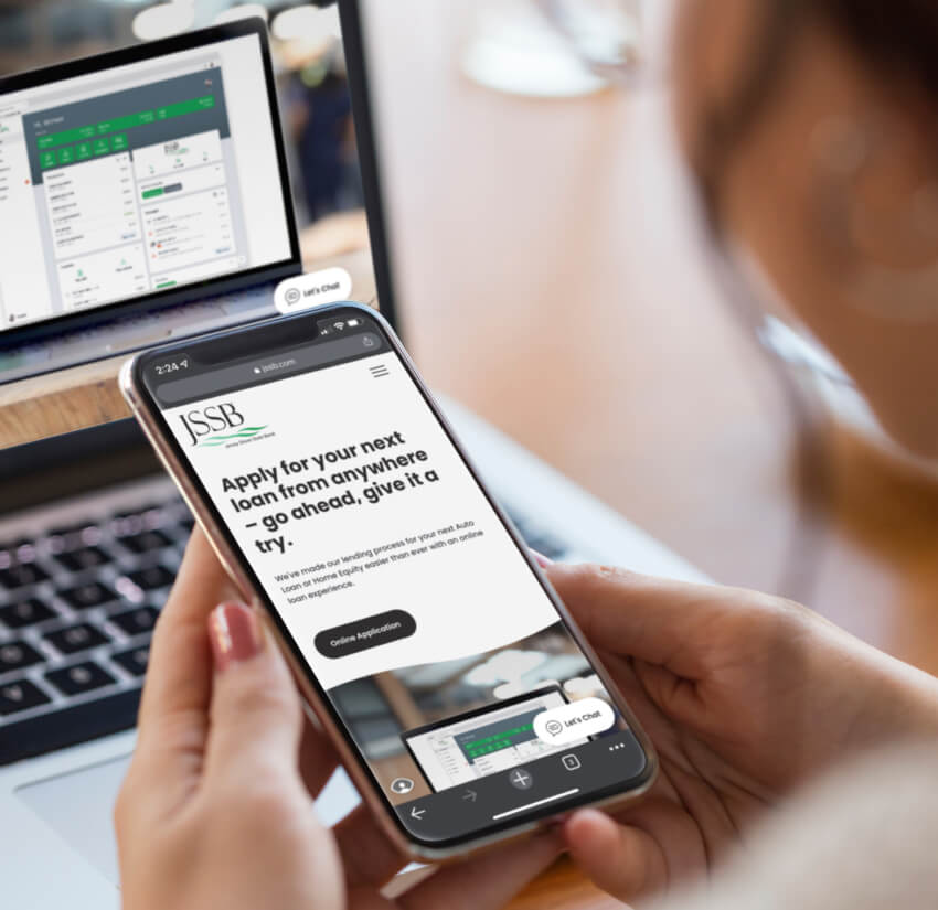 Woman holding phone that displays the Jersey Shore State Bank website while in the background the JSSB digital banking appears on a laptop.